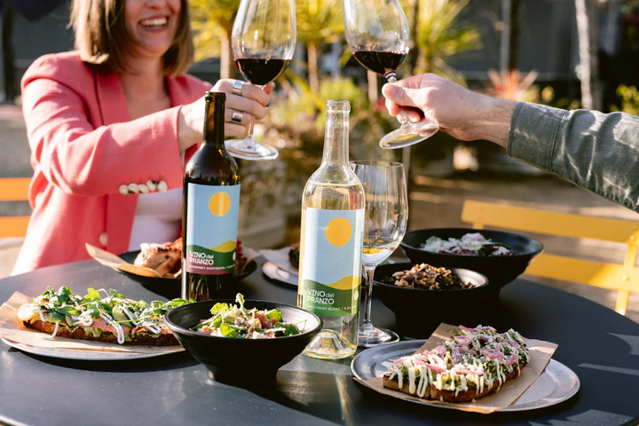 A couple enjoying wine and farm-to-table dishes outdoors, representing the Ultimate Napa Adventure Sweepstakes prize, a Napa Valley trip for two with tastings, activities, and travel included.