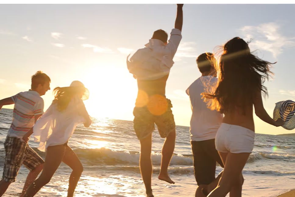 A group of friends running and jumping on the beach at sunset, capturing a carefree summer vibe used to promote the Founders Nonetheless Sweepstakes with a $5,000 cash prize. The image shows people celebrating by the ocean, matching a fun, feel-good sweepstakes theme for a Founders Brewing cash giveaway with a single online entry.