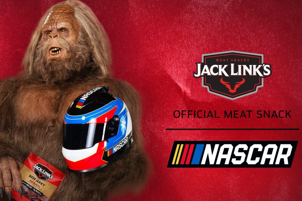 A Jack Link’s NASCAR sweepstakes promo image featuring a sasquatch holding a NASCAR racing helmet on a red background with the Jack Link’s logo and NASCAR logo. Jack Link’s Eat Meat Sweepstakes NASCAR giveaway graphic showing the mascot and race helmet, promoting NASCAR tickets and NASCAR race trip prizes. Jack Link’s NASCAR contest image highlighting the Jack Link’s brand, NASCAR branding, and the chance to win NASCAR race experiences and prize packs.
