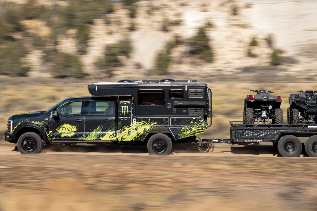 Black Ford F-250 towing a trailer with two ATVs for the Maverik Fuel Your Adventure Sweepstakes prize bundle, featuring a built-in camper adventure rig, utility trailer, and off-road vehicles in a desert landscape. Maverik sweepstakes image showing the grand prize Ford truck camper setup and ATV trailer combo for the Fuel Your Adventure giveaway. Outdoor road-trip style sweepstakes prize photo highlighting the Ford F-250 camper, trailer, and ATVs included in the Maverik adventure sweepstakes.
