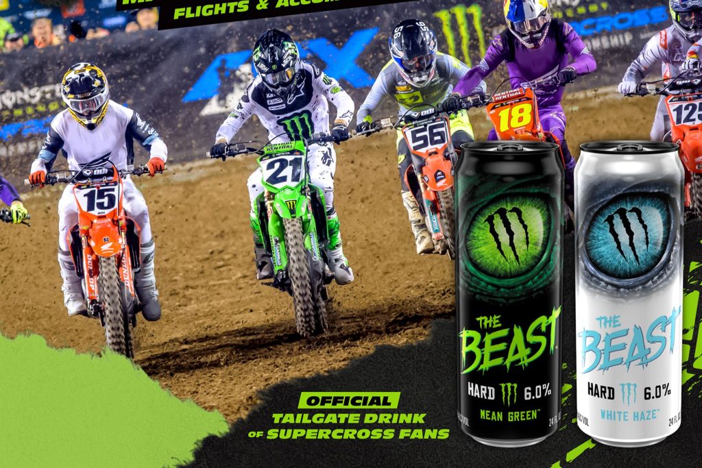 Four motocross riders race through a dirt turn during an AMA Supercross event with two Monster The Beast Hard Seltzer cans featured in the foreground. Action-packed supercross racing scene with riders on orange and green bikes, plus Monster The Beast Mean Green and White Haze cans shown as the promotional prize image for a Monster Brewing Company sweepstakes. Supercross tickets sweepstakes image featuring motocross racing, VIP finals trip giveaway, and Monster The Beast hard seltzer branding.