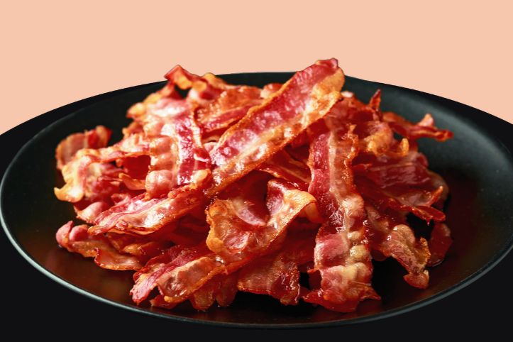 A stack of crispy cooked bacon strips piled high on a black plate, representing the grand prize of free bacon for a year in the Smithfield Win Free Bacon for a Year Sweepstakes. The image shows thick, sizzling bacon slices with rich red and golden tones, symbolizing a year’s supply of bacon awarded through manufacturer coupons. A heaping plate of crispy bacon strips illustrates the sweepstakes prize of 52 free bacon packages, highlighting the bacon giveaway and grocery prize.