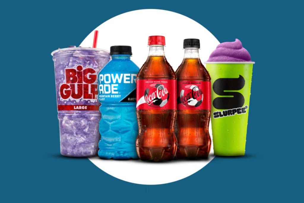 Promotional image showing qualifying 7-Eleven Scan Sip Score sweepstakes drinks including a Big Gulp cup, POWERADE bottle, Coca-Cola bottles, and a SLURPEE cup for the FIFA World Cup 26 fan experience sweepstakes and instant win game. The image highlights 7-Eleven and Speedway qualifying beverages used to earn entries and gameplays, featuring Coca-Cola, POWERADE, Big Gulp, and SLURPEE drinks tied to the Scan Sip Score instant win and sweepstakes promotion.