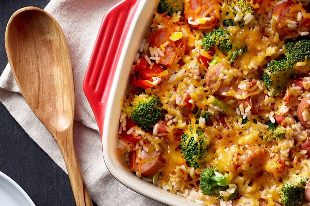 Overhead photo of a cheesy sausage-and-rice casserole with broccoli in a red baking dish, a cozy dinner-style image that fits the Eckrich Win Free Sausage for a Year Sweepstakes prize of smoked sausage coupons, free sausage giveaway, and year of sausage promotion.