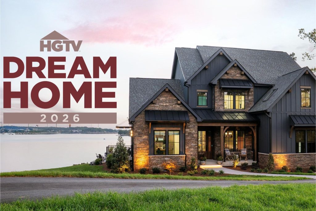 Exterior photo of the HGTV Dream Home 2026 showing a modern, dark-sided lakeside house with stone accents, warm exterior lighting, and a wide front porch at sunset. HGTV Dream Home 2026 sweepstakes prize image featuring the fully furnished waterfront home and grand prize package. Enter the HGTV Dream Home Giveaway 2026 for a chance to win the Dream Home in Charlotte, North Carolina plus cash.