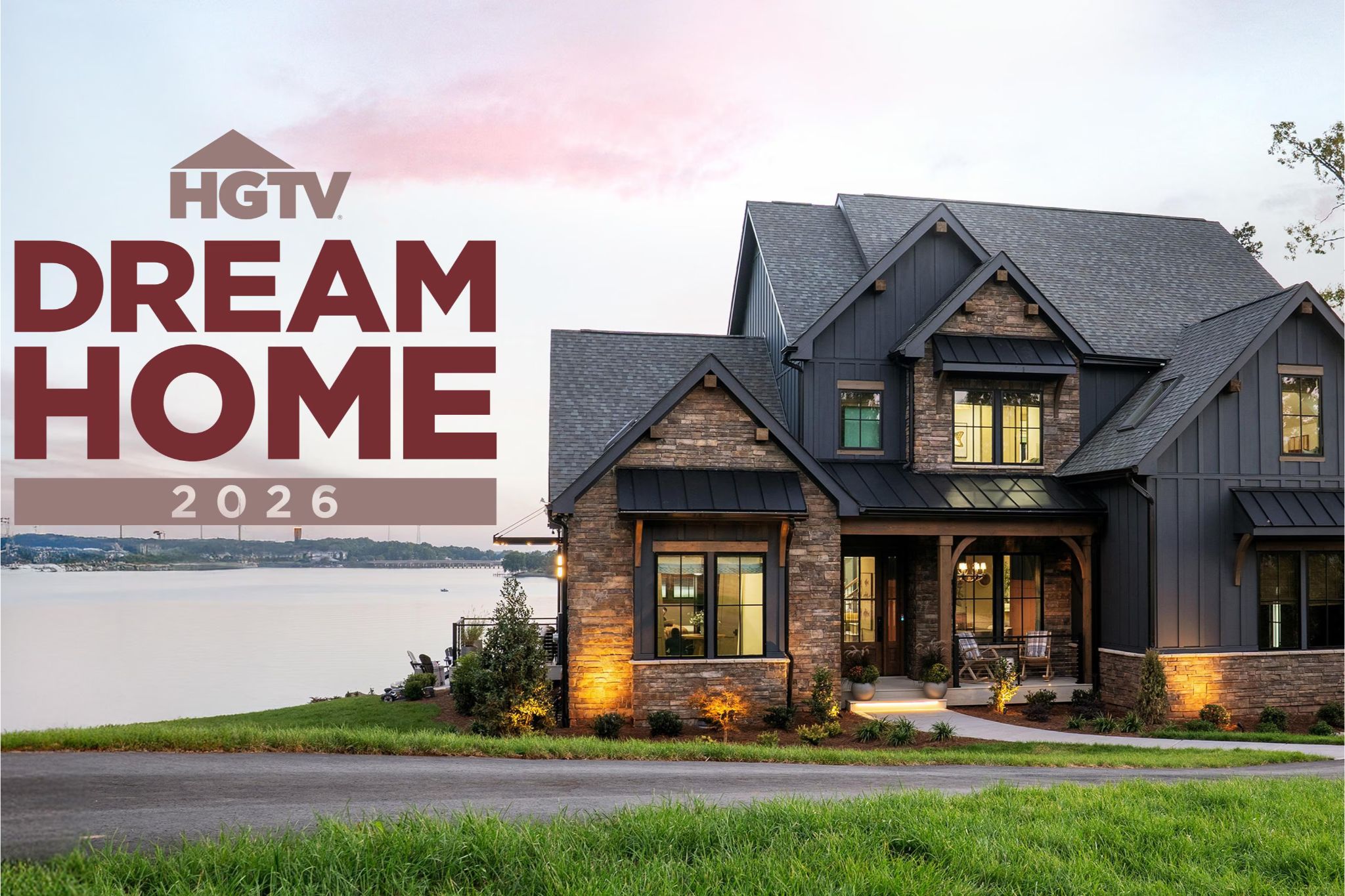 Exterior photo of the HGTV Dream Home 2026 showing a modern, dark-sided lakeside house with stone accents, warm exterior lighting, and a wide front porch at sunset. HGTV Dream Home 2026 sweepstakes prize image featuring the fully furnished waterfront home and grand prize package. Enter the HGTV Dream Home Giveaway 2026 for a chance to win the Dream Home in Charlotte, North Carolina plus cash.
