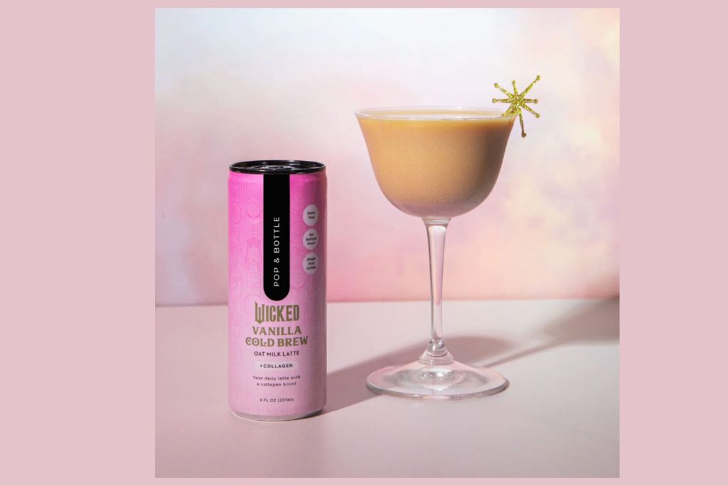 A pink can of Pop and Bottle Wicked Vanilla Cold Brew oat milk latte with collagen sits beside a frothy espresso martini in a coupe glass against a soft pastel background. The ready-to-drink vanilla cold brew can is displayed next to a creamy coffee cocktail styled for a Wicked-themed watch party. The image features Pop and Bottle canned cold brew coffee and an espresso martini recipe presentation, highlighting the Wicked Sweepstakes prize theme.