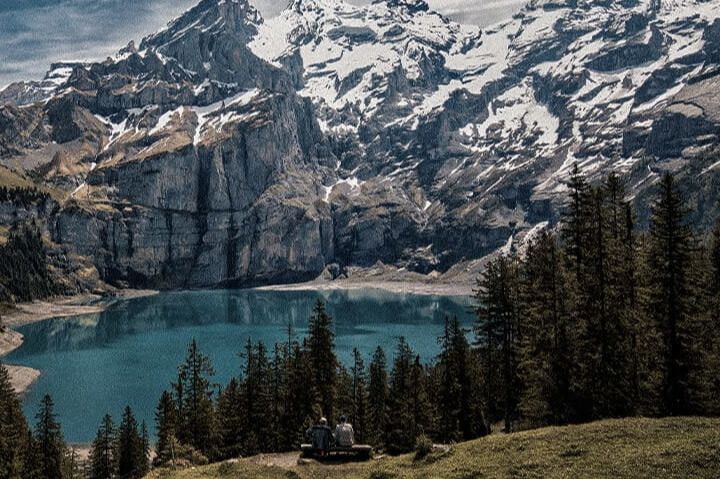 Snowy Swiss Alps mountain landscape above a blue alpine lake promoting the SWISSGEAR win a trip to Switzerland sweepstakes, a travel giveaway for a Switzerland ski trip for two with airfare, train tickets, ski passes, luggage, and a $1,000 travel stipend.