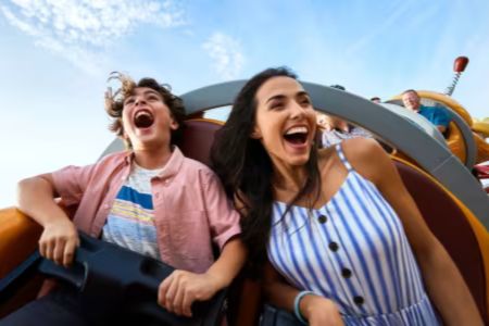 Two people laughing on a roller coaster at an Orlando theme park, capturing the excitement of a family vacation getaway to Orlando with theme park thrills, hotel stay, and airfare included. The image shows a joyful theme park ride experience that represents a 5-day Orlando family vacation prize with flights, SeaWorld tickets, Aquatica admission, and hotel accommodations in Florida.