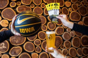 Big Grove Game Time Ticket Giveaway 2026 image showing hands holding an Iowa Hawkeyes basketball and a game day ticket giveaway card next to a poured beer. Promotional photo for Big Grove Brewery Hawkeyes ticket sweepstakes featuring Iowa basketball, beer, and ticket giveaway branding for Hawkeyes men’s and women’s games.