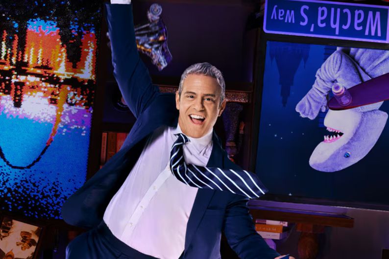 Excited TV host celebrating in a colorful late-night talk show set resembling a clubhouse studio, representing the Bravo Watch What Happens Live Sweepstakes grand prize trip to New York City and a live show taping experience. Image illustrating a TV studio environment with bright lights, bookshelves, and stage decor tied to the Watch What Happens Live taping prize. Promotional image symbolizing the chance to attend a live Bravo talk show recording and win a New York City travel experience.