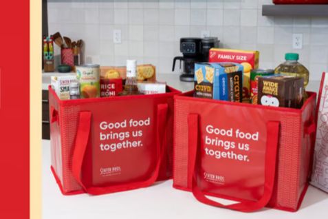 Two red reusable grocery tote bags filled with pantry items and household groceries on a white kitchen counter, representing the Free Groceries Giveaway with Stater Bros. Markets gift cards for groceries all year. Bright kitchen scene showing stocked grocery bags and everyday food staples, illustrating a win free groceries for a year prize awarded as gift cards. Red shopping totes packed with cereal, snacks, and pantry goods to visualize the Stater Bros. grocery gift card sweepstakes prize.