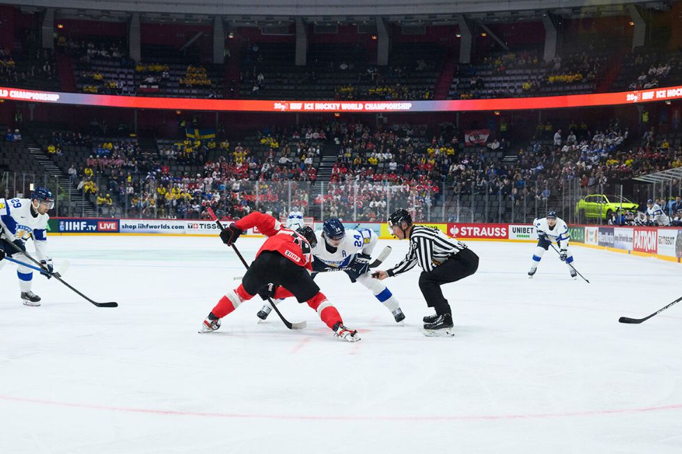 A thrilling ice hockey face-off occurs between players in red and blue jerseys, while a referee watches closely, surrounded by an excited crowd in the arena, featured in the Nokian Tyres IIHF Ice Hockey World Championship Trip Giveaway