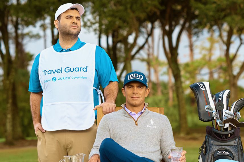 A golfer relaxes in a chair on the course while a caddy stands beside him, both enjoying the outdoors. Golf clubs are positioned nearby, hinting at a leisurely game ahead, featured in the Zurich Classic Sweepstakes