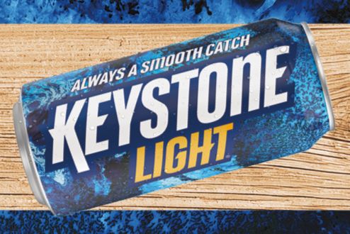 A close-up of a Keystone Light beer can resting on a wooden surface, showcasing its vibrant blue design and bold white text against an aquatic background, featured in the Keystone Light Fishing Sweepstakes