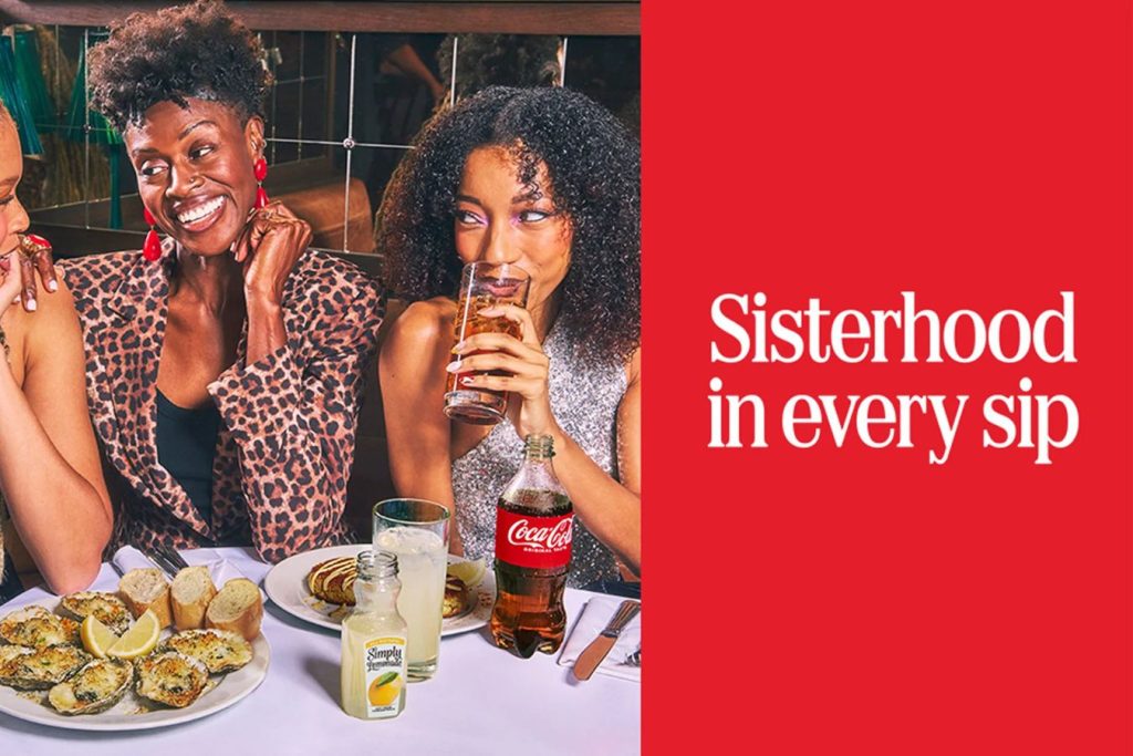 Three women enjoy a lively meal together, sharing laughter and drinks amidst plates of food, with a focus on their camaraderie and joyful moments, featured in the Coca-Cola Essence Festival Sweepstakes