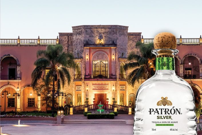 A grand building with vibrant landscaping and palm trees stands under a clear sky, featuring a large entryway and intricate architecture, with a bottle of Patrón Silver tequila prominently displayed in the foreground, featured in the Hacienda PATRÓN Sweepstakes