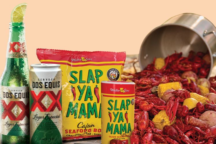 A refreshing green bottle of beer, two cans, and a packet of Cajun seasoning are displayed in front of a spread of crawfish, corn, and sausage on a light background, featured in the Dos Equis Crawfish Sweepstakes