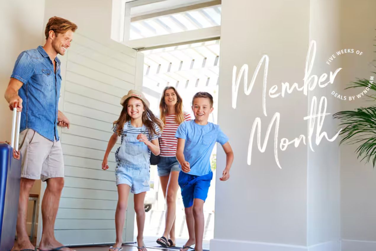 A man enters a bright, modern hallway carrying a suitcase while two children run ahead excitedly. A woman follows, smiling, creating a joyful family scene, featured in the Wyndham Rewards 2026 Member Month Sweepstakes