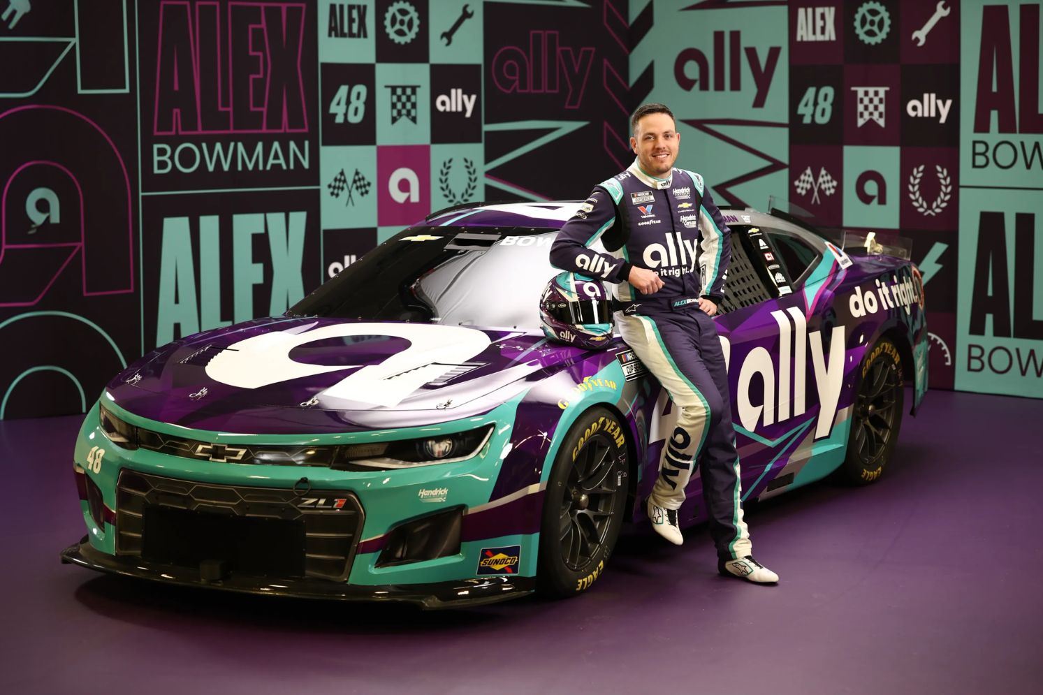 Alex Bowman stands confidently next to his vibrant NASCAR Chevy, featuring a bold purple, teal, and black design, against a colorful backdrop showcasing his name and number, featured in the Ally Alex Bowman Refer-A-Friend Sweepstakes