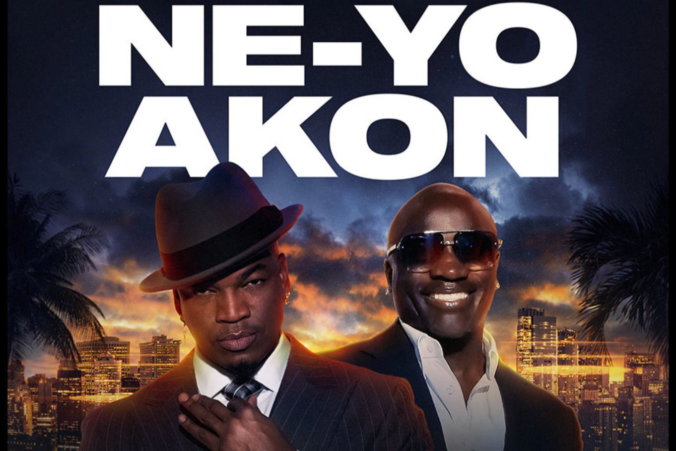 Two male artists pose confidently against a vibrant city skyline at sunset, with one wearing a stylish fedora and the other in sunglasses, both exuding charisma and style, featured in the On with Mario Lopez NE-YO AKON Flyaway Sweepstakes