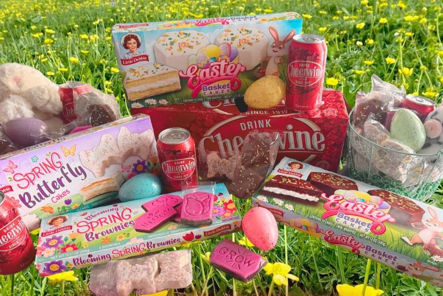 A colorful arrangement of Easter-themed sweets, including cakes and brownies, is set against a backdrop of vibrant green grass and yellow flowers, creating a festive spring scene, featured in the Cheerwine Little Debbie Spring Giveaway