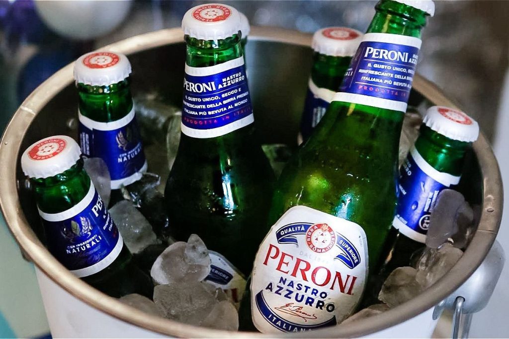 A silver ice bucket filled with an assortment of green beer bottles and ice, showcasing chilled beverages ready for serving, featured in the Peroni Nastro Azzurro 0.0% Las Vegas Race Weekend Sweepstakes