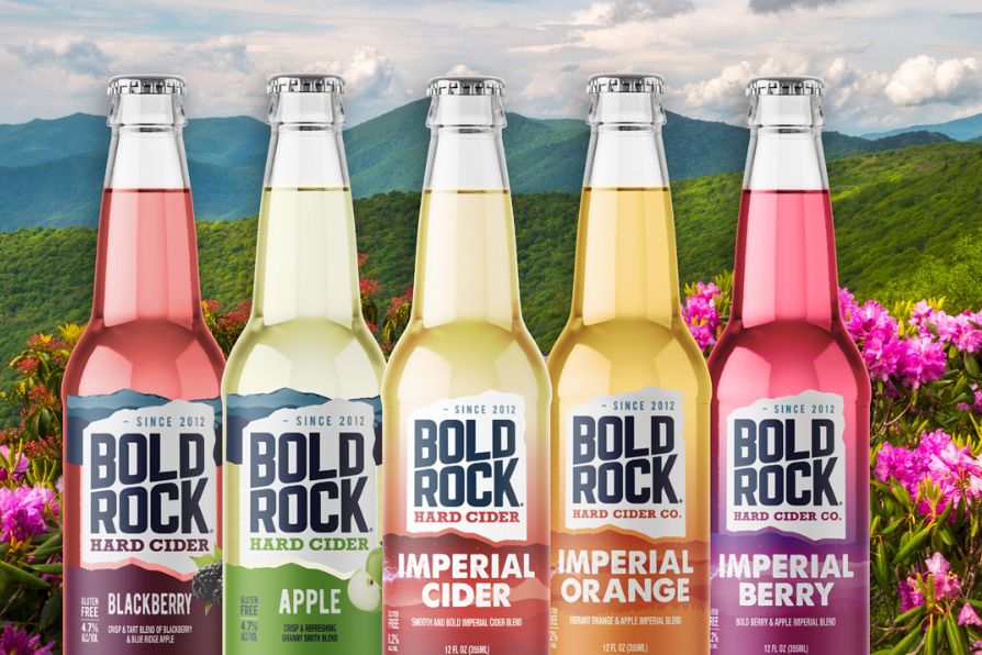 A vibrant assortment of Bold Rock hard ciders in glass bottles sits against a picturesque mountain backdrop adorned with colorful flowers, highlighting various fruit flavors, featured in the Bold Rock Getaway Sweepstakes