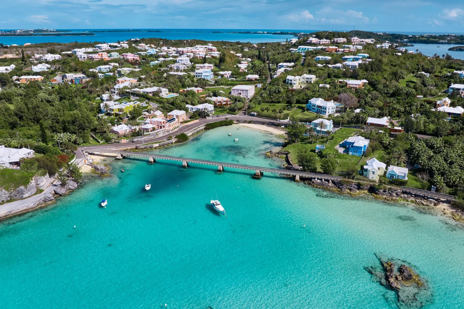 Aerial view of a picturesque coastal area featuring turquoise waters, a small bridge, and charming homes surrounded by lush greenery on a sunny day, featured in the Bermuda Getaway Sweepstakes