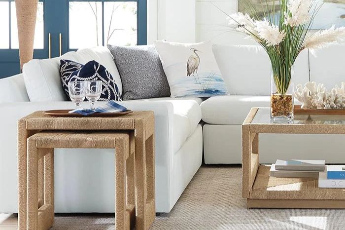 A bright, stylish living room features a white sectional sofa adorned with decorative pillows and small wooden tables, complemented by a vase of flowers and natural decor on the coffee table, featured in the Ethan Allen $2,500 Gift Card Sweepstakes