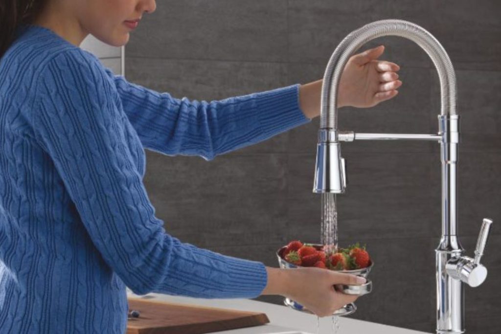 A person in a blue sweater rinses strawberries in a metal bowl under a modern kitchen faucet, with water flowing down and a wooden cutting board in the background, featured in the Delta $3,500 Kitchen Upgrade Sweepstakes