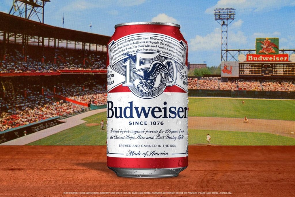 A cold can of beer stands on a wooden surface, with a baseball stadium and a crowd in the background, capturing the spirit of a sunny game day, featured in the Budweiser Field of Dreams Sweepstakes