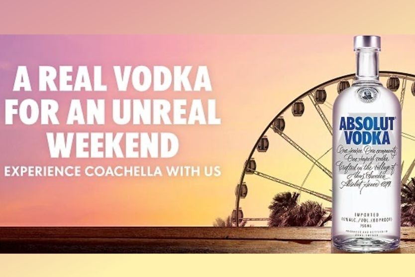 A clear bottle of vodka is prominently displayed in front of a colorful sunset and a Ferris wheel, suggesting a festive atmosphere perfect for a weekend experience, featured in the Absolut Coachella Sweepstakes