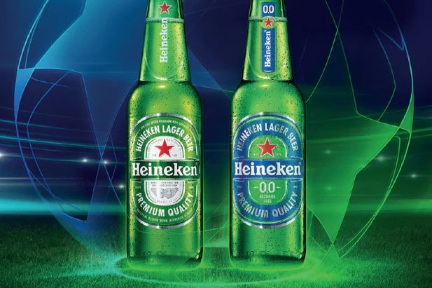 Two green bottles of Heineken beer, one regular and one non-alcoholic, are displayed against a vibrant blue and green background, evoking a sporty and energetic atmosphere, featured in the Heineken UEFA Champions League Sweepstakes