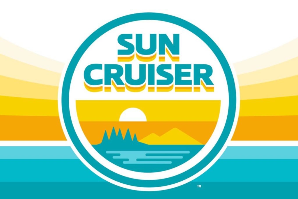 A vibrant, stylized logo featuring a sun setting over mountains and water, framed by a circular border with the text "SUN CRUISER" prominently displayed. Bright colors evoke a cheerful atmosphere, featured in the Sun Cruiser Jazz Fest Sweepstakes