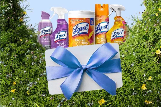 A collection of Lysol cleaning products is arranged against a backdrop of lush greenery, accompanied by a gift box adorned with a blue bow, suggesting a gift-giving theme, featured in the Lysol Sweepstakes