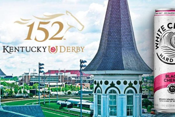 The iconic spire of Churchill Downs rises against a clear sky, overlooking the racetrack, with a can of spiked seltzer prominently positioned in the foreground, featured in the White Claw Kentucky Derby Tickets Sweepstakes
