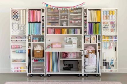 A well-organized craft space features a large white storage unit filled with colorful supplies like ribbons, papers, and sewing materials, showcasing a sewing machine at the center, featured in the Create Room DreamBox Sweepstakes