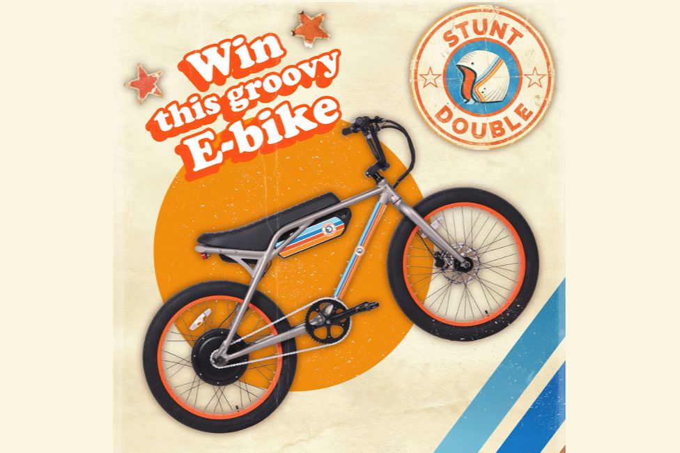 A stylish e-bike with a sleek design and orange accents is prominently displayed against a retro background with circular patterns and star decorations, featured in the Stunt Double E-Bike Sweepstakes