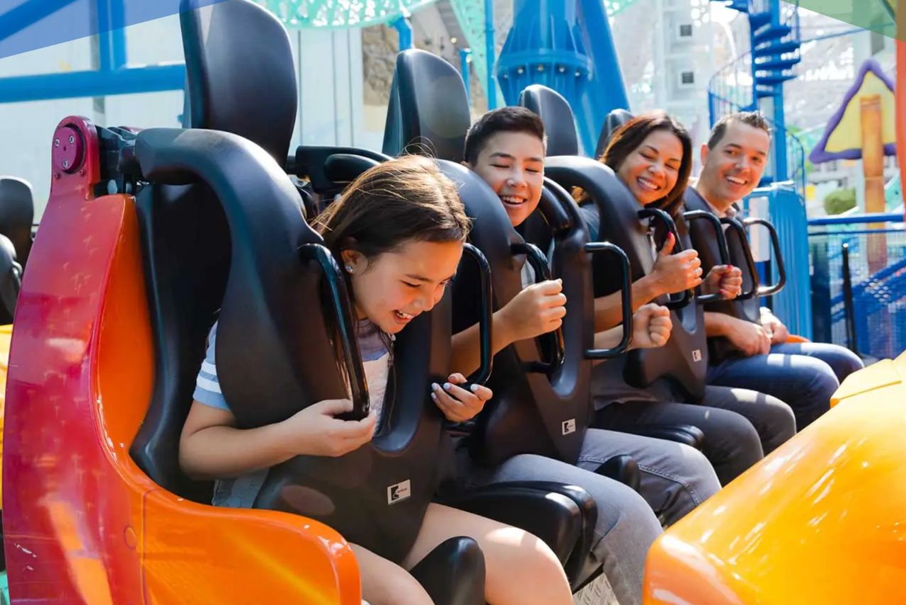 A group of four excited individuals, including a girl and a boy, enjoy the anticipation of a thrill ride, seated securely with their harnesses fastened, smiling and ready for fun, featured in the Bloomington Mall of America Gift Card Sweepstakes