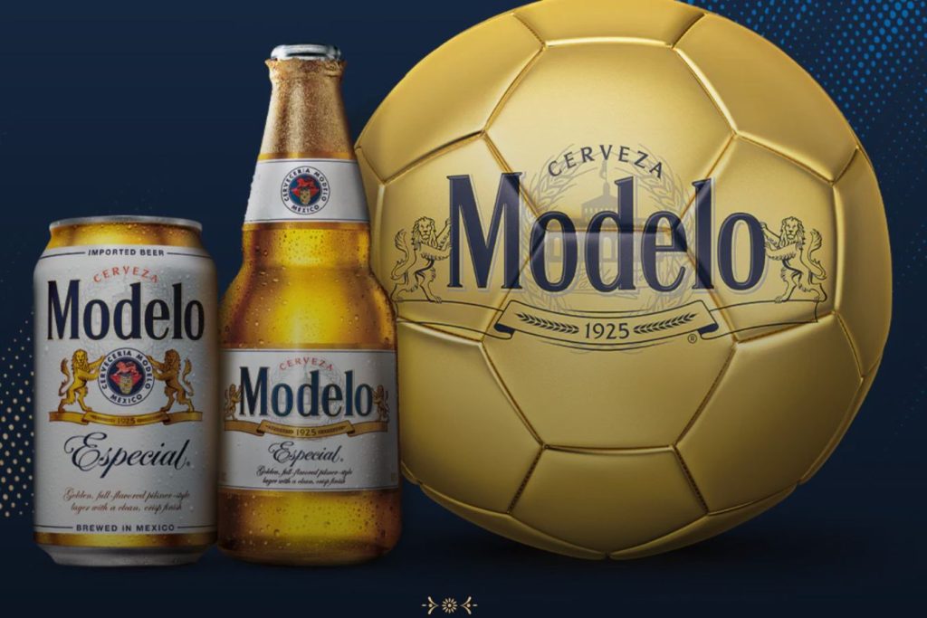 Two bottles of beer and a can are arranged beside a shiny gold soccer ball, showcasing a vibrant promotional display, featured in the Modelo Soccer Sweepstakes