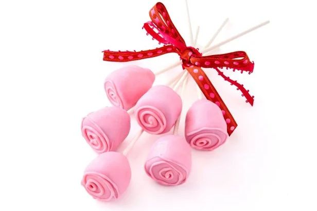 A bouquet of pink rose-shaped cake pops tied with a vibrant red ribbon, elegantly arranged on white sticks against a bright background, featured in the Food Network Magazine Name This Dish Sweepstakes