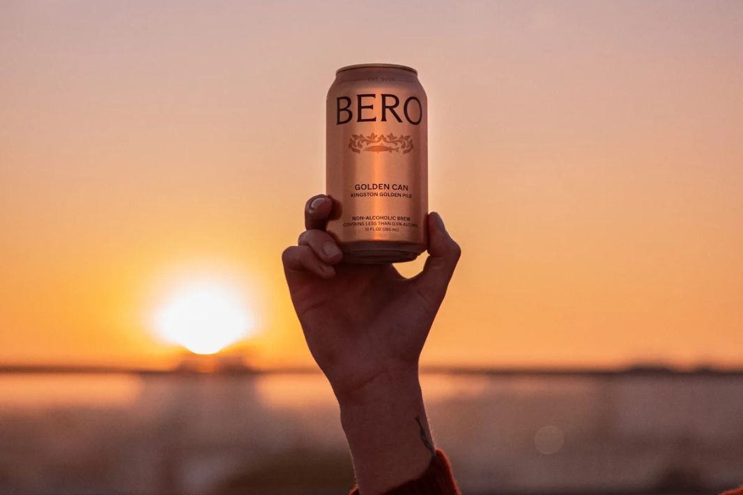 A hand lifts a golden can against a vibrant sunset, capturing a moment of celebration and relaxation in the fading light of day, featured in the Bero Golden Can Sweepstakes