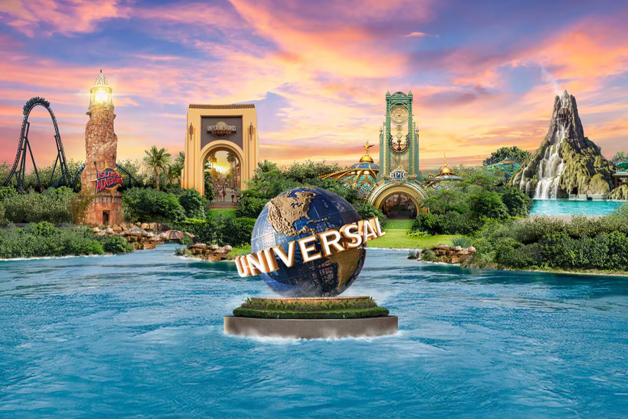 A scenic view features a globe surrounded by lush greenery, iconic theme park structures, a roller coaster, and a waterfall under a vibrant sunset sky, evoking excitement and adventure, featured in the Fandango Universal Adventure Getaway Sweepstakes