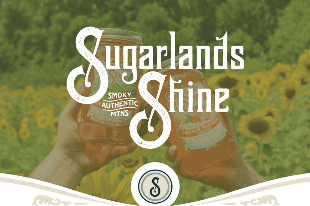 Hands hold two jars labeled "Orange Squeeze" amidst a vibrant field of sunflowers, creating a cheerful, summery atmosphere, featured in the Sugarlands Distiller for a Day Sweepstakes