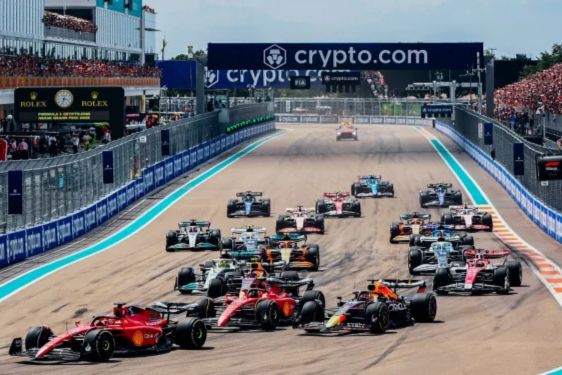 A thrilling Formula 1 race is underway with multiple cars, including red and blue ones, competing fiercely on a sunlit track, surrounded by enthusiastic spectators, featured in the Ticketmaster Miami Grand Prix Rooftop Suite Sweepstakes