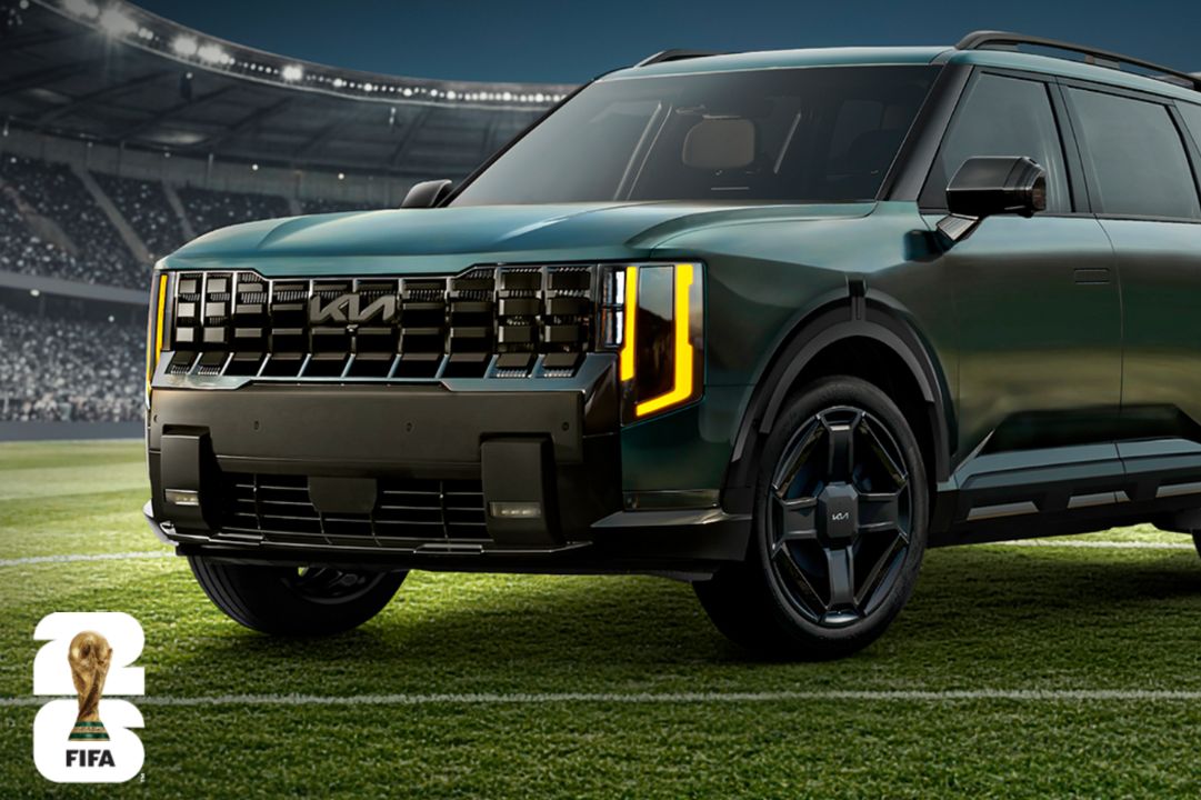 A sleek green SUV stands on a vibrant football field, showcasing its bold front grille and striking headlights, set against a backdrop of a packed stadium ready for action, featured in the Kia FIFA World Cup 2026 Sweepstakes