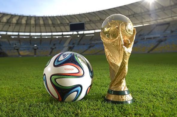 A soccer ball rests on the grass next to the FIFA World Cup trophy, set against the backdrop of an empty stadium under bright lighting, featured in the AXE FIFA World Cup Sweepstakes