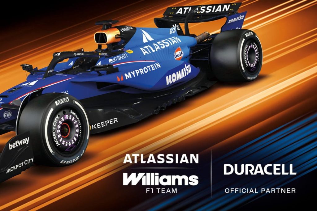 A sleek Formula 1 car in blue and orange, featuring bold sponsorship graphics, is set against a dynamic background of orange and black streaks, highlighting its racing design, featured in the Duracell Williams Racing Sweepstakes