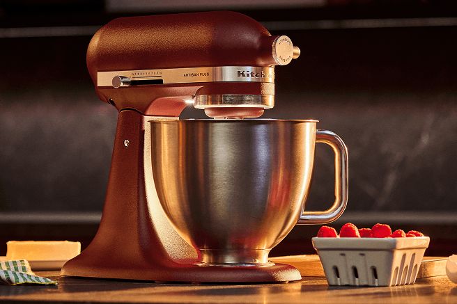 A rich brown stand mixer sits on a countertop beside a bowl filled with raspberries, showcasing a warm kitchen atmosphere perfect for baking and cooking, featured in the KitchenAid Artisan Plus Sweepstakes
